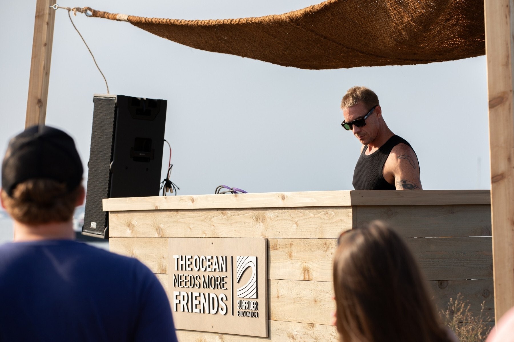 Diplo djing in front of a sign that reads "The ocean needs more friends."