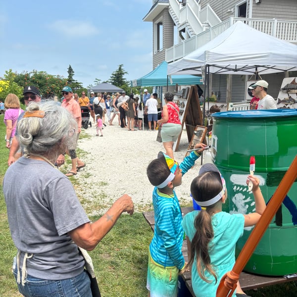 Carol and kids painting a rain barrel green and white for the Harbor Fest event.
