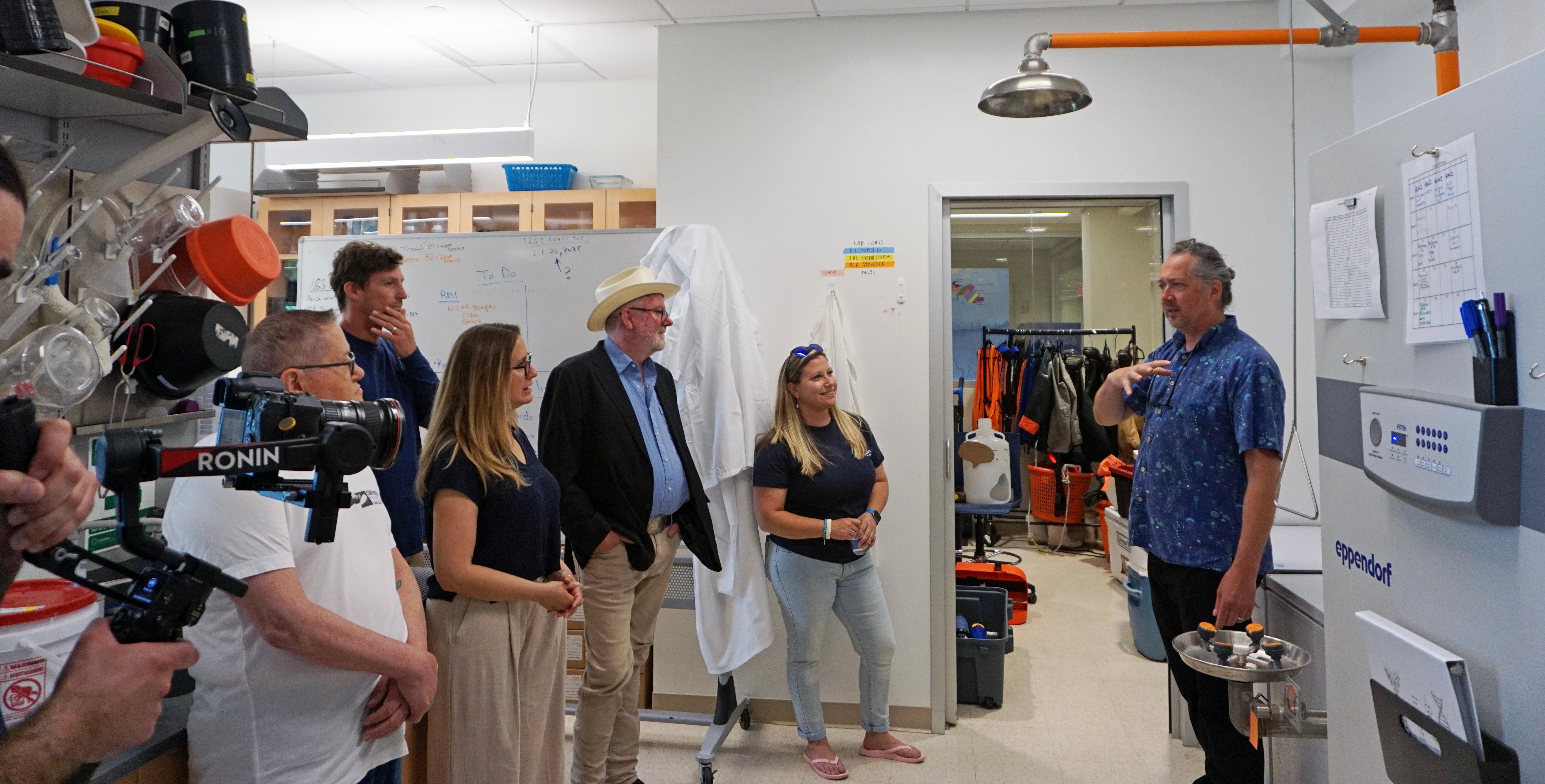 Professor Jason Adolf speaks to the press in the lab during the&nbsp;partnership launch ceremony, alongside representatives from the Surfrider Foundation and Monmouth University.