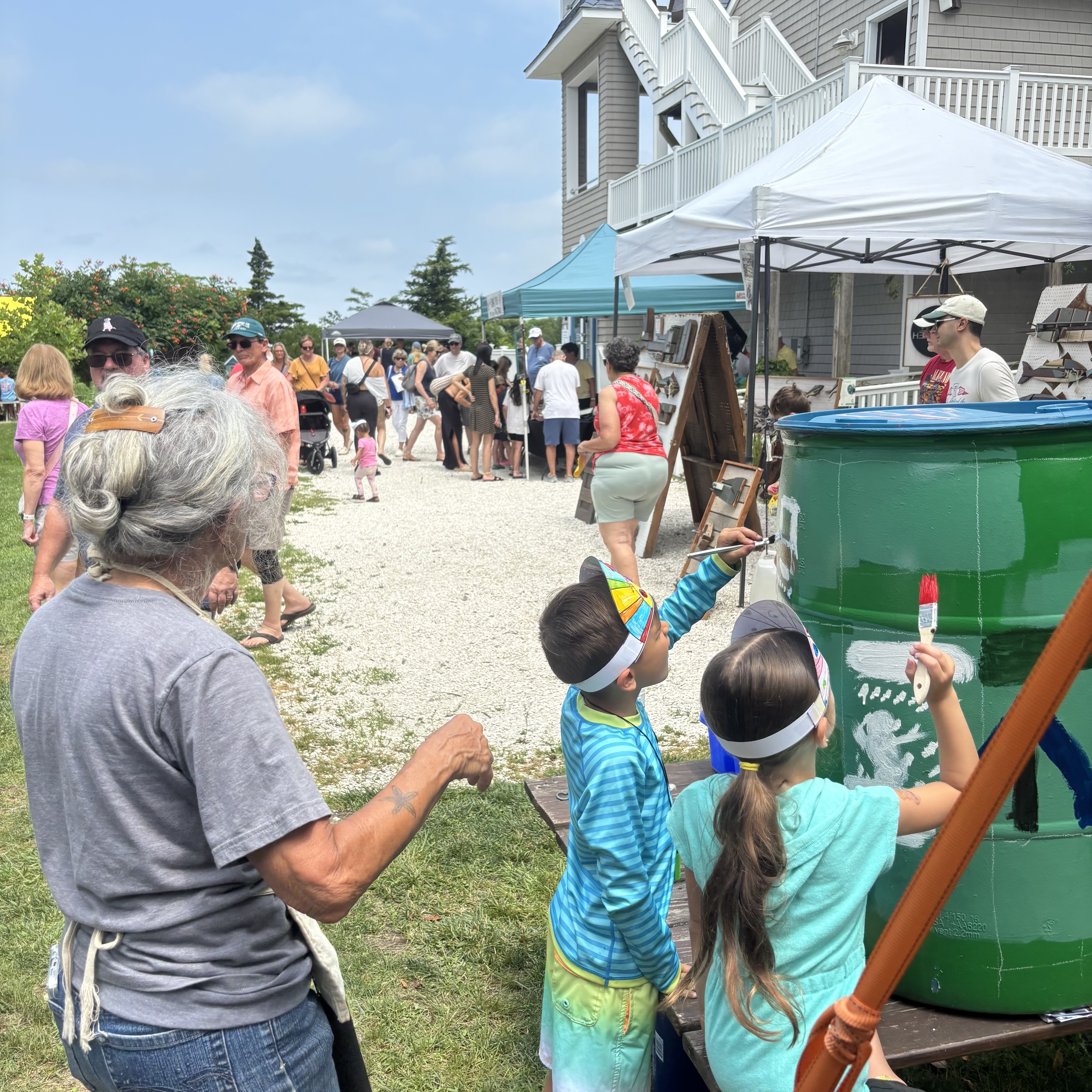 Carol and kids painting a rain barrel green and white for the Harbor Fest event.